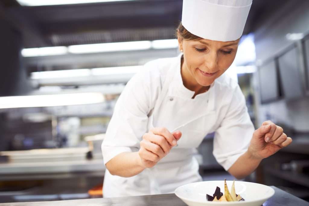 Köchin in einer Restaurantküche dekoriert einen Speisenteller, Foto: envato elements